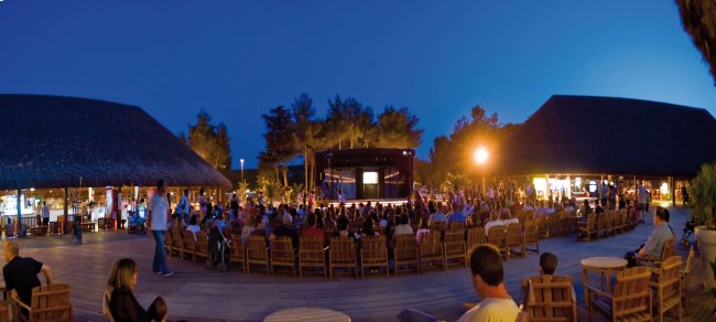Persone sedute attorno a un palco all'aperto di sera.