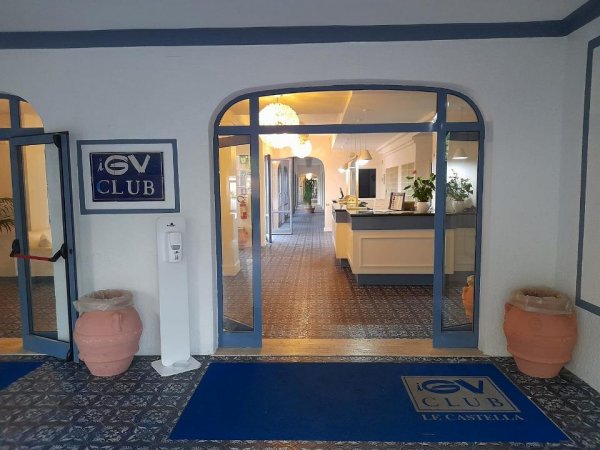 Entrata di un club con tappeto blu e insegna, reception visibile all'interno.