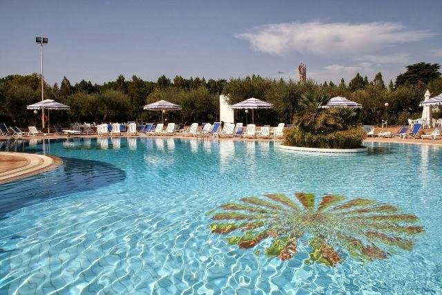 Piscina con sdraio e ombrelloni, circondata da alberi.