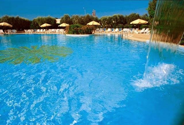 Piscina con cascata d'acqua, ombrelloni e lettini intorno.