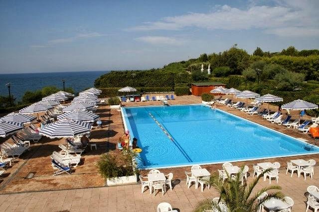 Piscina all'aperto con lettini e ombrelloni a righe.