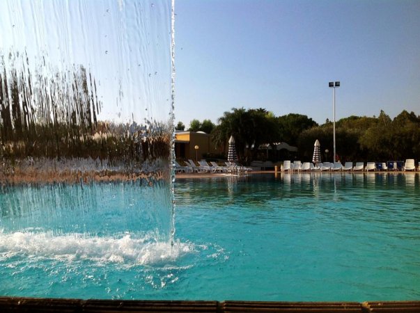 Cascata d'acqua in una piscina con lettini sullo sfondo.