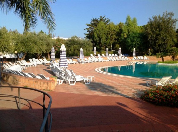 Piscina circondata da lettini e ombrelloni a righe bianche e blu.