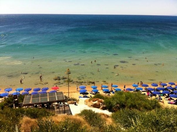 Spiaggia con ombrelloni blu e mare trasparente, vista dall'alto.