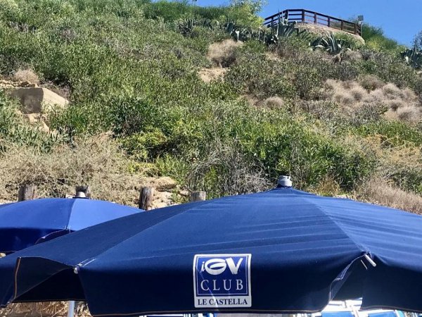Ombrelloni blu di un club con collina verde sullo sfondo.