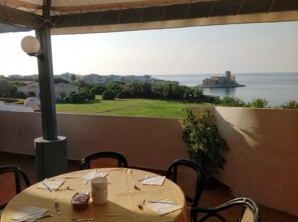Tavolo apparecchiato su terrazza con vista su prato e mare.