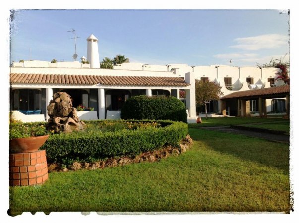 Un edificio bianco con tetto in tegole, circondato da un giardino verde curato.
