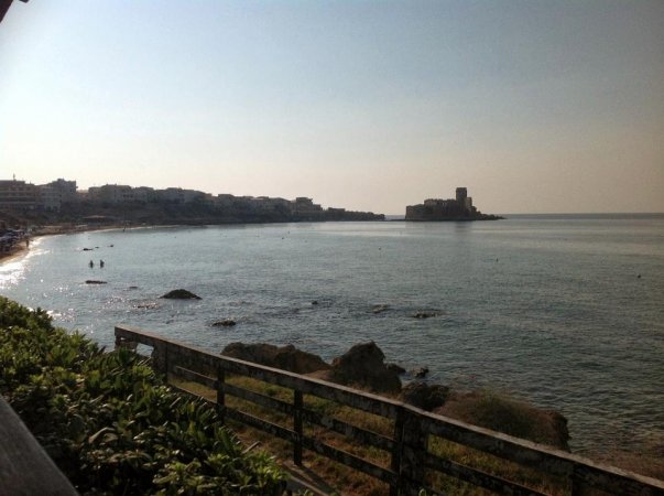 Vista su un mare calmo con una spiaggia a sinistra e un castello in lontananza.