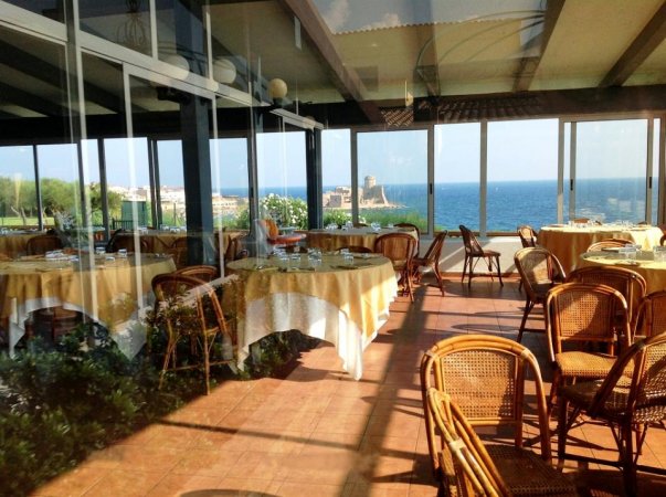 Ristorante con grandi vetrate vista mare, tavoli apparecchiati e sedie in rattan.