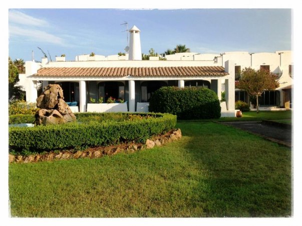 Una casa bianca con tetto in tegole e un giardino ben curato con siepi e rocce.
