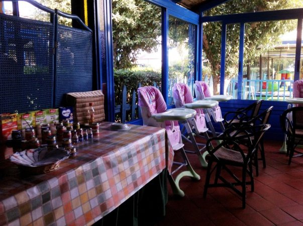 Una veranda con seggioloni per bambini, un tavolo con tovaglia a quadri e prodotti per bambini.