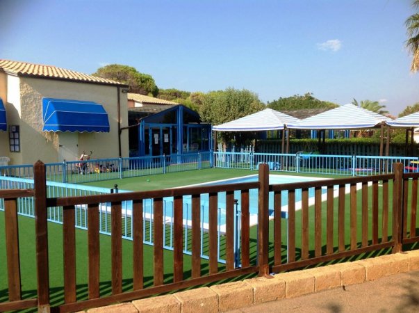 Area esterna con piscina recintata, tende blu e verdeggianti dintorni.