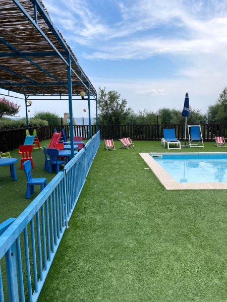 Piscina con sdraio colorate e area giochi coperta da tettoia di legno.