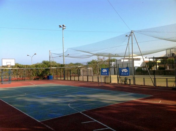 Un campo sportivo con basket e reti protettive, attrezzato per diversi sport.