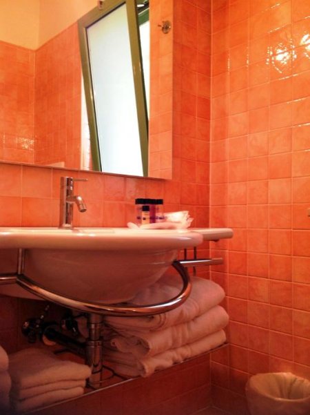 Bagno con piastrelle arancioni, lavandino bianco e asciugamani sotto.