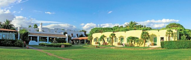 Edifici bianchi e gialli immersi nel verde con cielo blu e alcune nuvole.