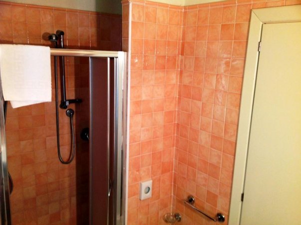 Bagno con piastrelle arancioni, doccia moderna e asciugamano bianco.