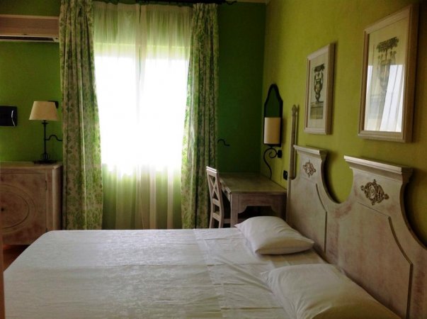 Camera da letto con pareti verdi, tenda chiara e mobili in legno chiaro.