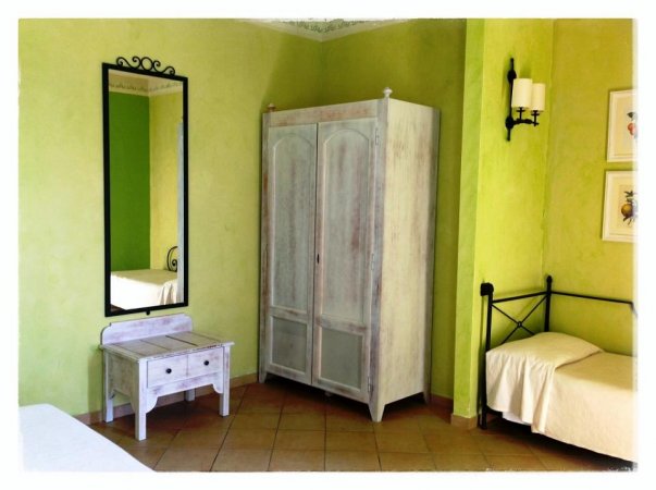 Camera da letto con armadio bianco, specchio a muro e letto singolo, su pareti verde chiaro.