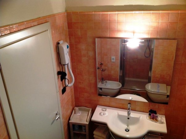 Bagno con piastrelle arancioni, lavabo con specchio e asciugacapelli a muro.