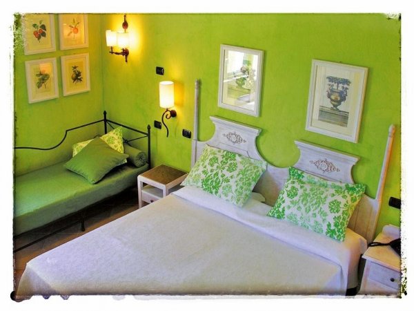 Camera da letto verde con letto matrimoniale, divano letto e quadri alle pareti.
