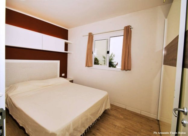 Camera da letto con parete rossa, letto matrimoniale e finestra con tende beige.