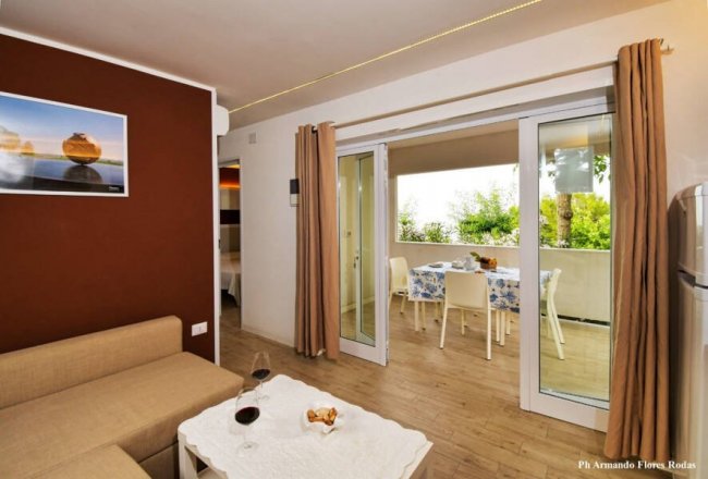 Soggiorno con divano beige, tavolino e accesso alla terrazza con tavolo da pranzo.