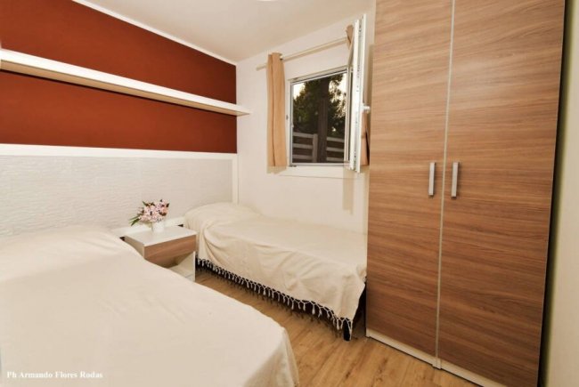 Camera con due letti singoli, armadio in legno chiaro e finestra con tende beige.