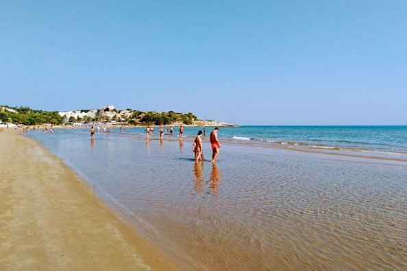 Persone camminano sulla battigia di una spiaggia sabbiosa.