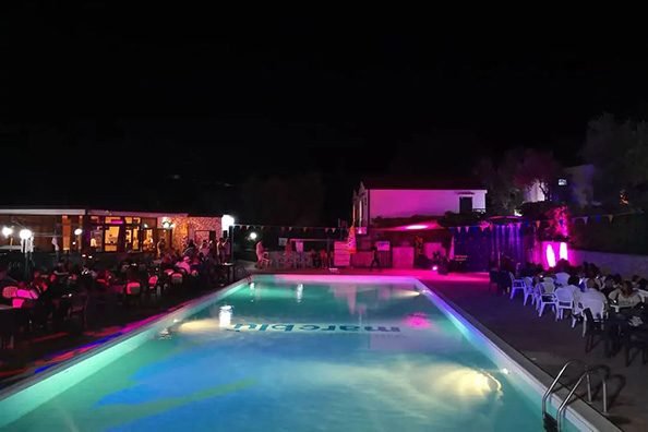 Piscina illuminata di notte con luci rosa intorno.