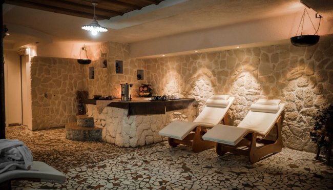 Area relax con lettini e parete in pietra illuminata.