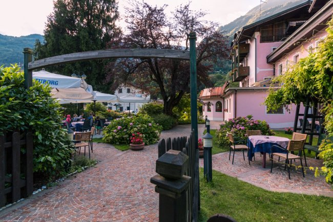 Giardino con tavoli e sedie, arco in legno e cespugli fioriti.