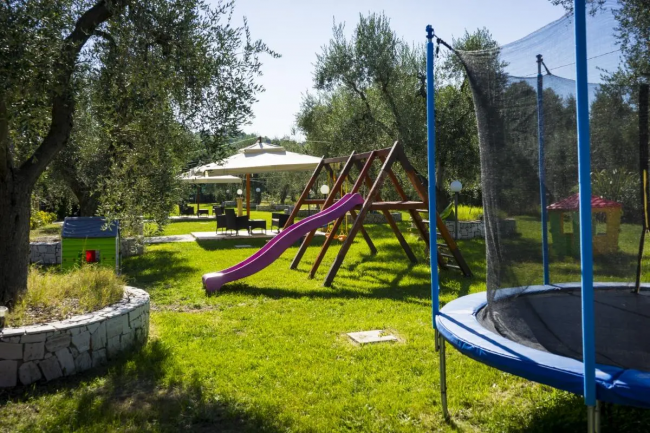 Giardino con trampolino, scivolo viola e tavoli sotto un gazebo.