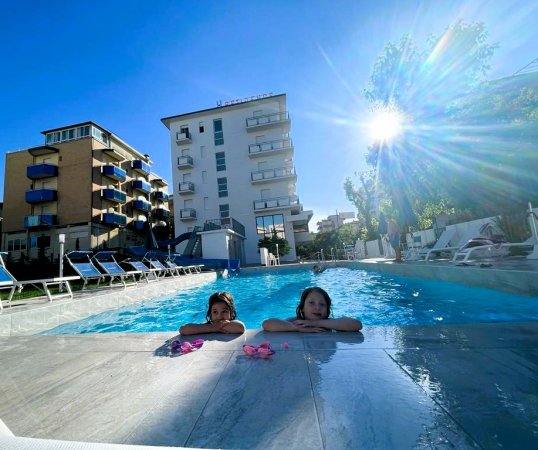 Due bambini in piscina con sole splendente.
