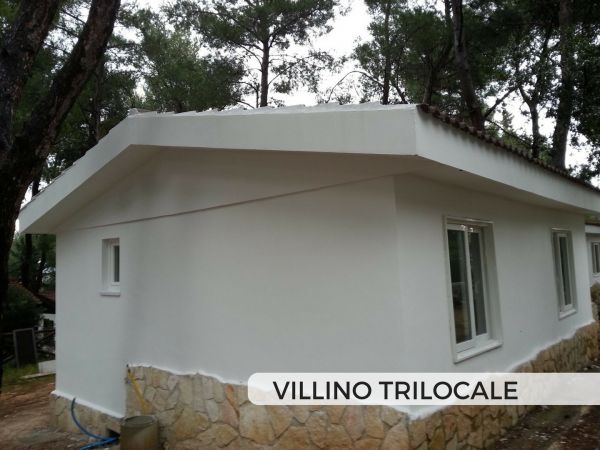 Villino bianco con base in pietra in un'area alberata.