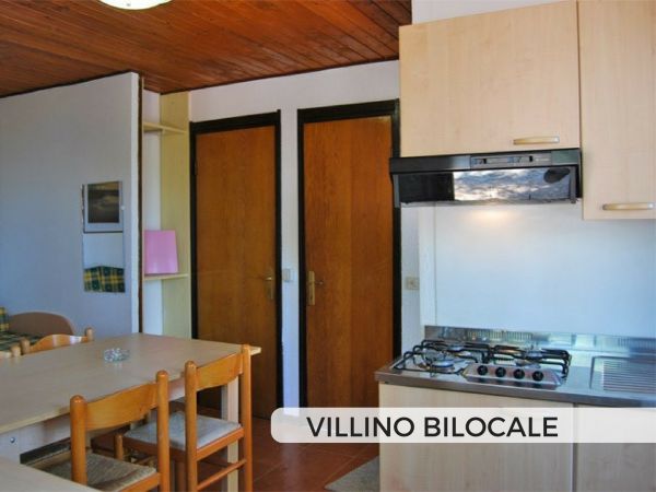 Cucina con tavolo e sedie, due porte chiuse dietro.
