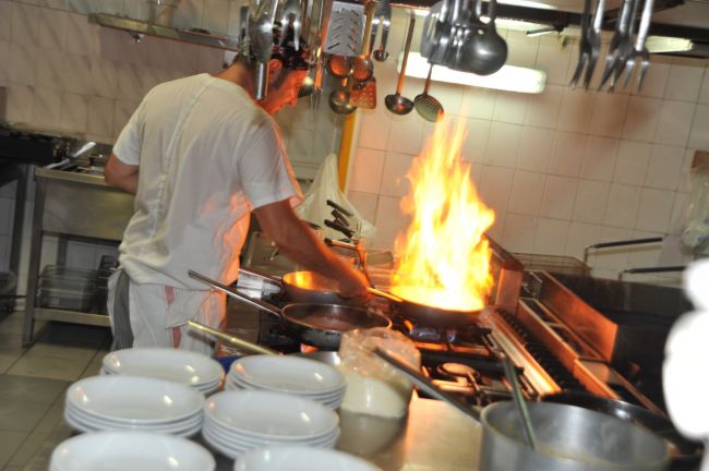 Cuoco in cucina con padella fiammeggiante.