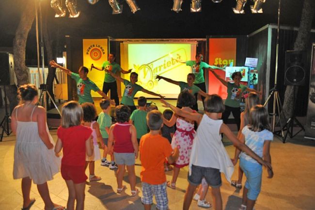 Bambini ballano davanti a un palco con animatori.