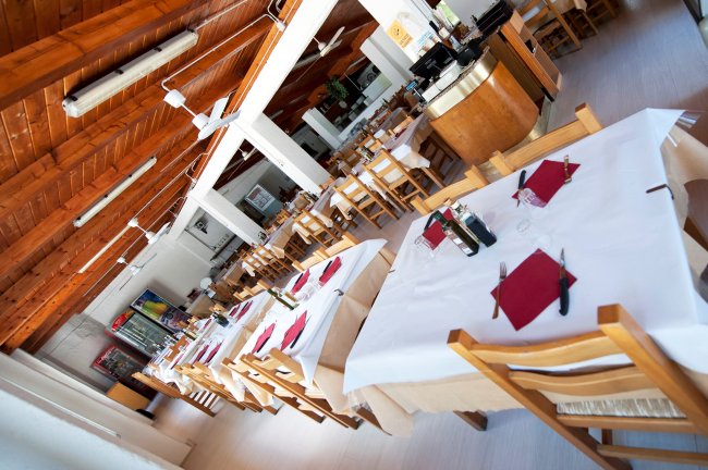 Interno di un ristorante con tavoli apparecchiati e soffitto in legno.