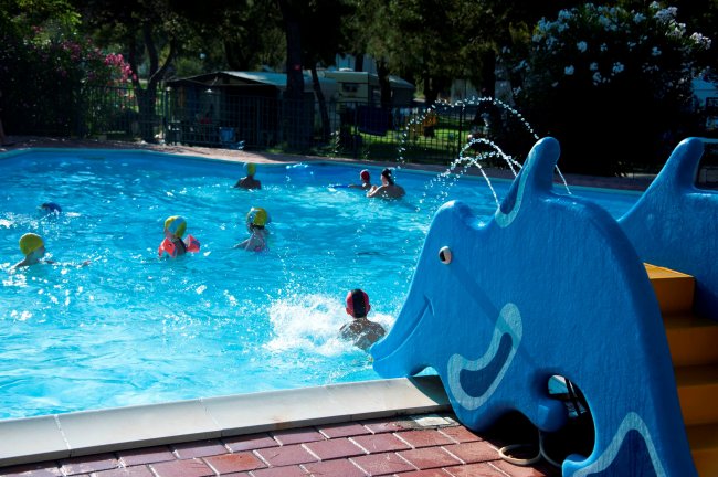 Bambini giocano in piscina con scivolo a delfino.