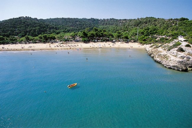 Baia con acqua turchese e barca gialla in lontananza.