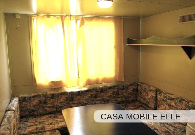 Interno di una casa mobile con divano ad angolo e tavolo.