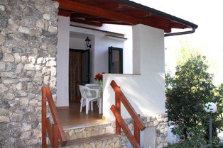 Veranda con pareti in pietra, tavolo e sedie bianche.
