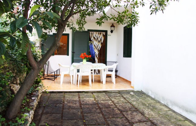 Patio esterno con tavolo, sedie bianche e albero.