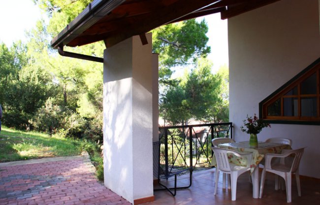 Veranda con tavolo e sedie bianche, vista sul giardino alberato.