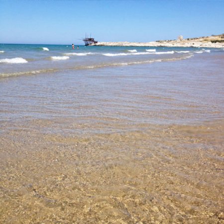 Spiaggia con acqua limpida e una nave in lontananza.