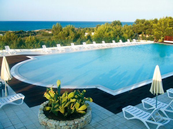 Piscina con lettini bianchi e vista sul mare.