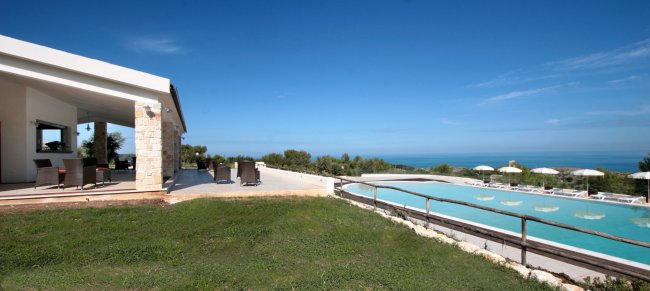 Piscina e prato con mare in lontananza.