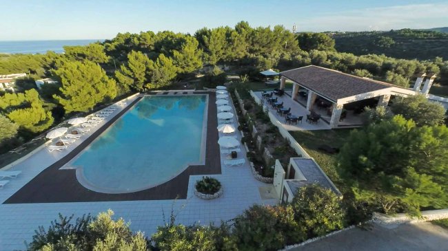 Piscina con ombrelloni e un edificio coperto accanto.