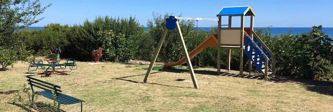 Parco giochi con altalena e scivolo vicino al mare.